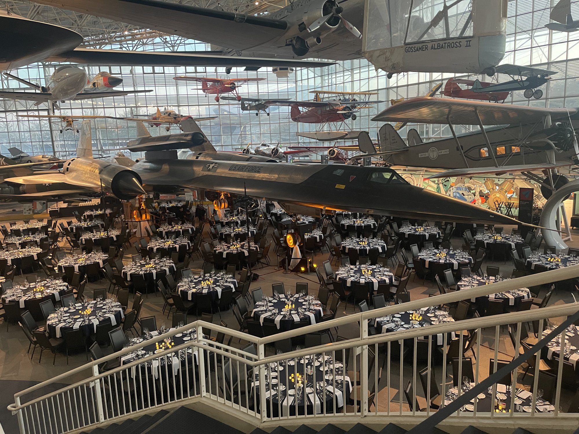 A formal banquet in an aviation museum with vintage aircraft suspended above the tables